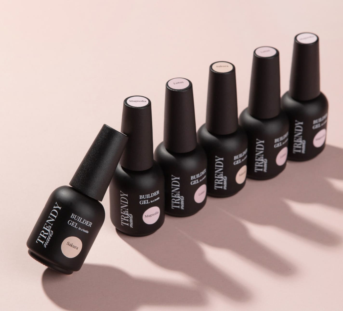 Row of Trendy Nails Builder Gel bottles in black matte finish with shades labeled, displayed on a pink background.